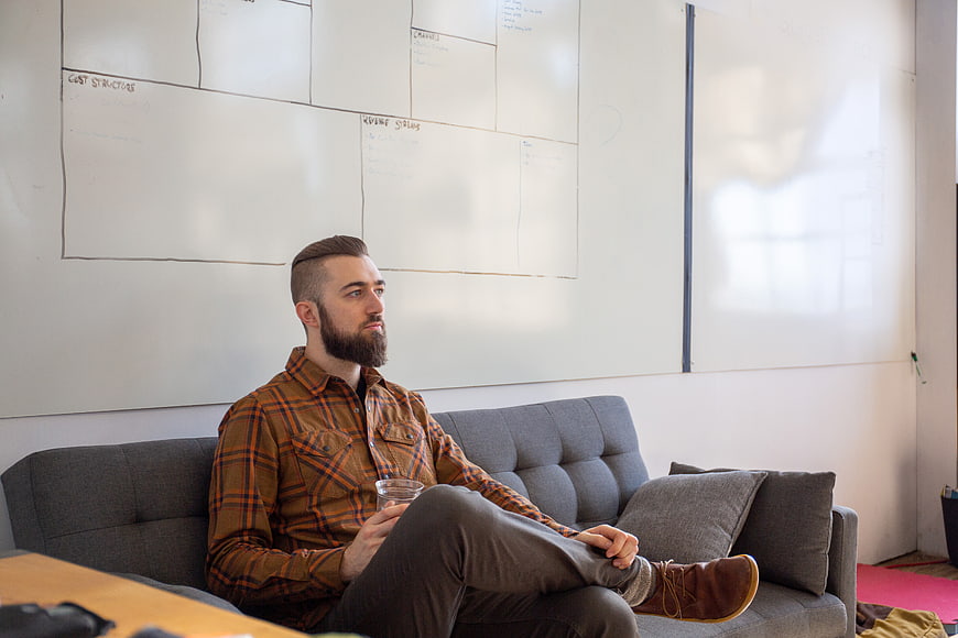 Thoughtful man sitting on couch in creative office with whiteboard