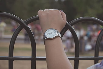 Woman's wrist with silver watch on black metal fence