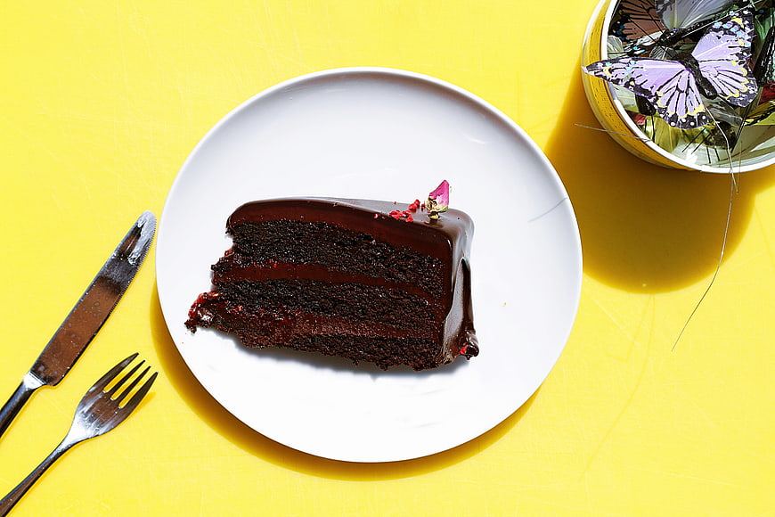 Slice of chocolate cake on white plate with yellow background