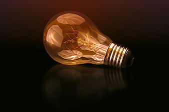 Illuminated vintage light bulb lying on a dark reflective surface