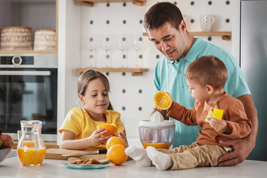 Father and children making fresh orange juice in kitchen