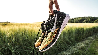 Hand holding Nike running shoes in a green grassy field