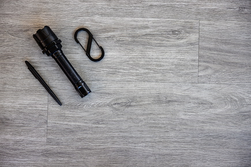 Black flashlight, carabiner, and pen on gray wood background