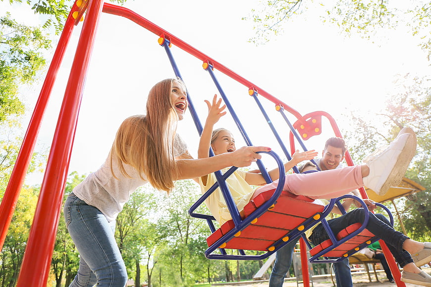 Happy family playing on swings in sunny park