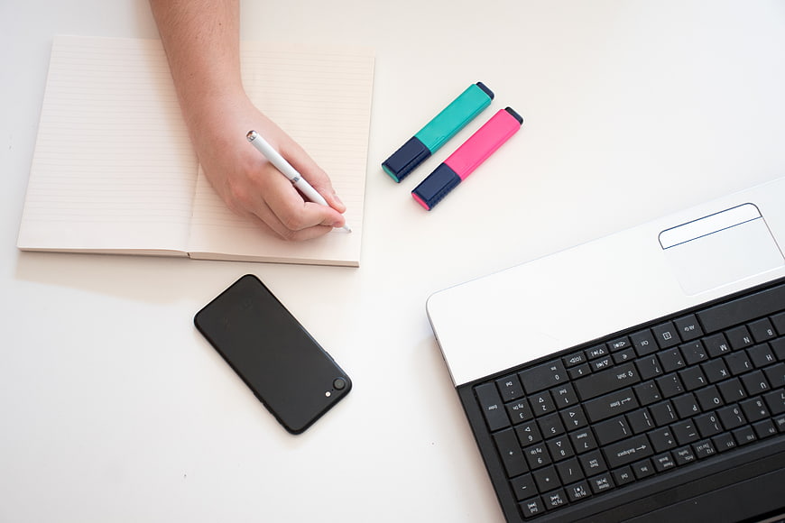 Flat lay of hand writing in notebook with laptop and smartphone