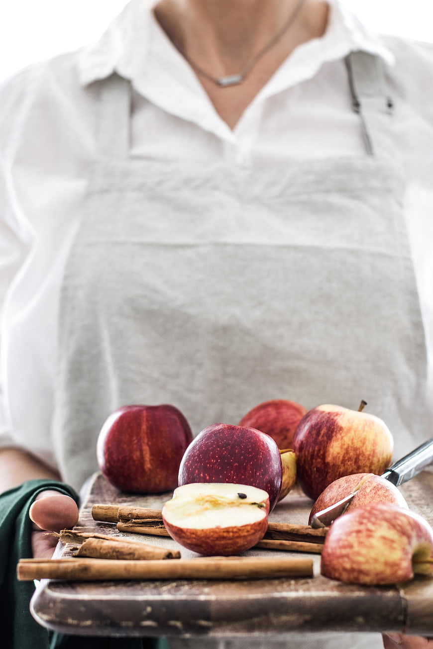 Woman in apron holding tray of fresh apples and cinnamon