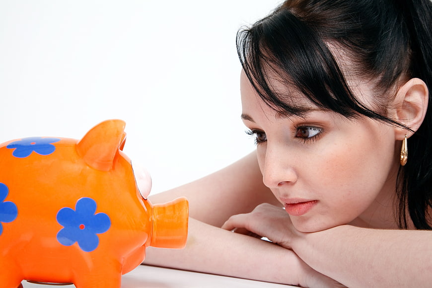 Young Woman Looking at Orange Piggy Bank on White Background