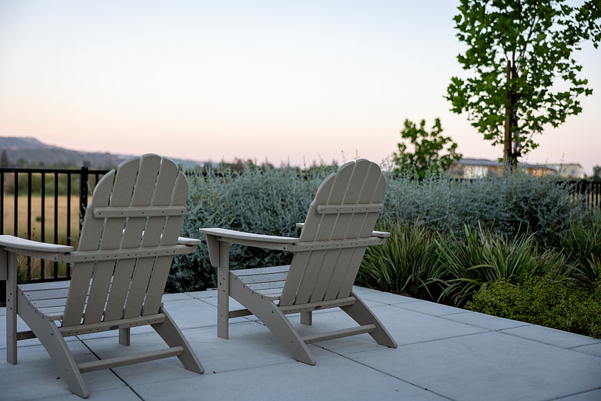 Two beige Adirondack chairs on a patio at dusk