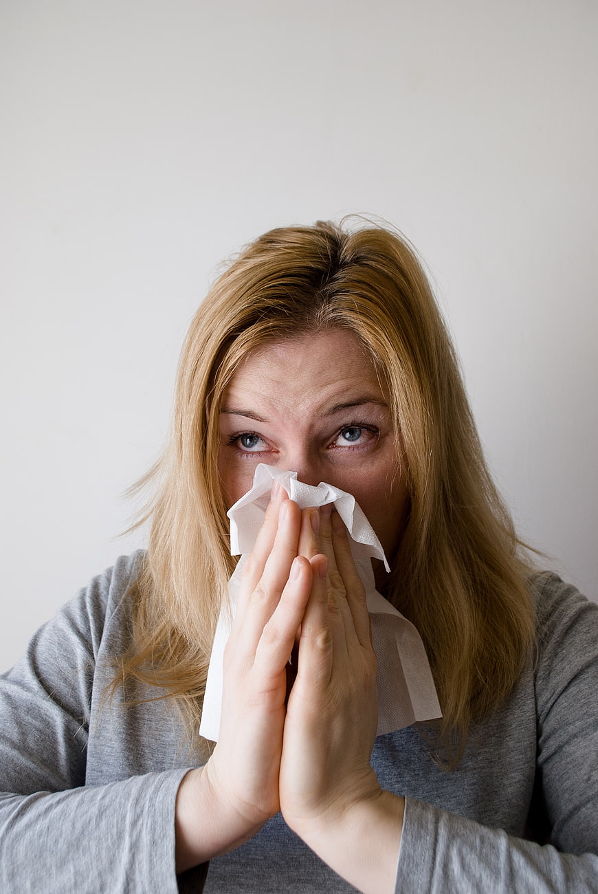 Blonde woman blowing nose with tissue against white background