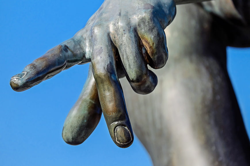 Close-up of bronze hand sculpture against blue sky