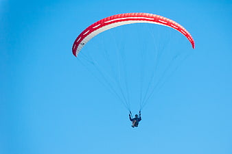 Paraglider with Red Canopy Flying Against Clear Blue Sky