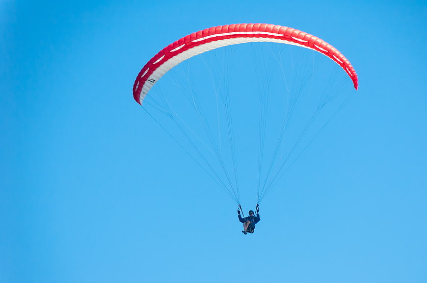 Paraglider with Red Canopy Flying Against Clear Blue Sky