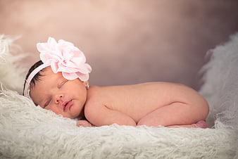 Sleeping newborn baby girl wearing pink flower headband on soft white fur
