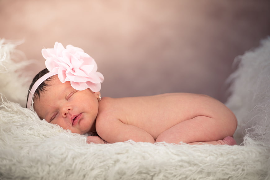Sleeping newborn baby girl wearing pink flower headband on soft white fur