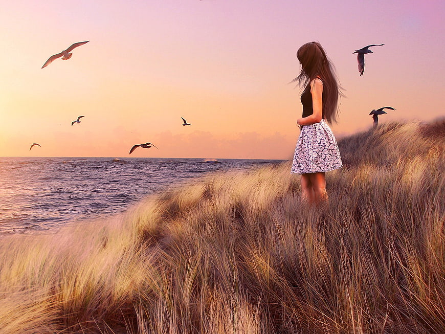 Woman in Floral Dress Standing on Dune at Sunset