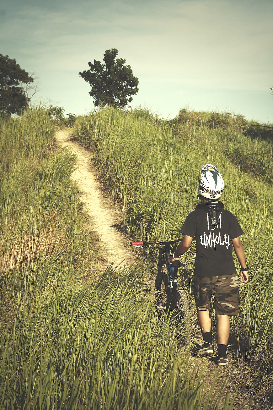 Mountain biker walking bike on grassy trail