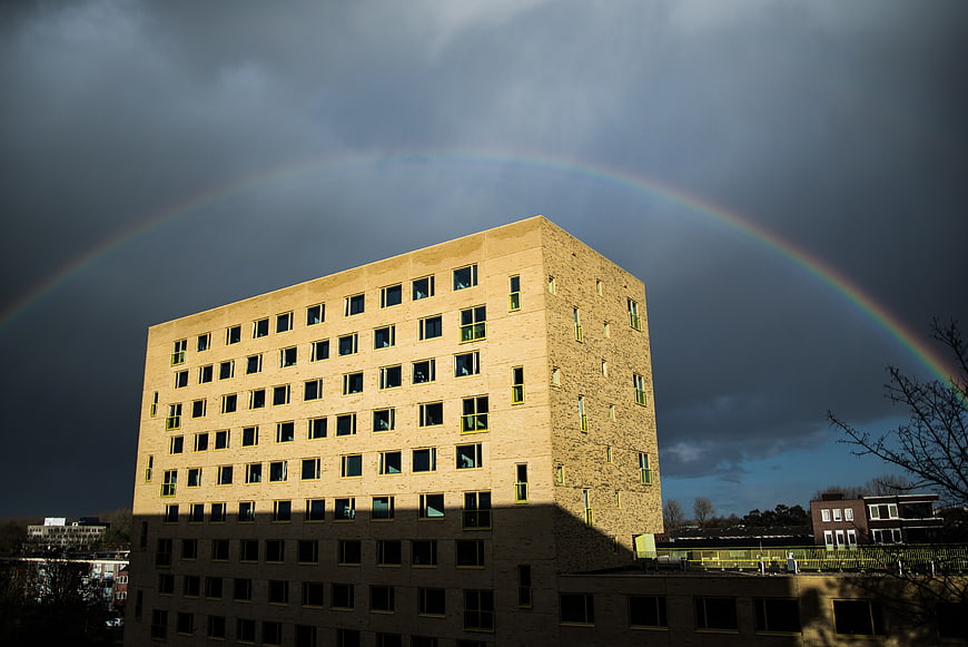 Modern beige building with rainbow arching over dark stormy sky