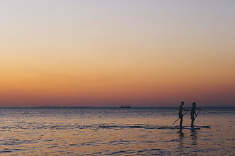 Silhouettes of two people paddleboarding at sunset on calm ocean