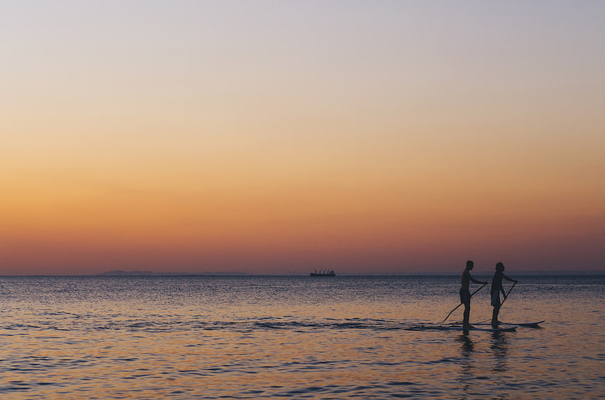 Silhouettes of two people paddleboarding at sunset on calm ocean