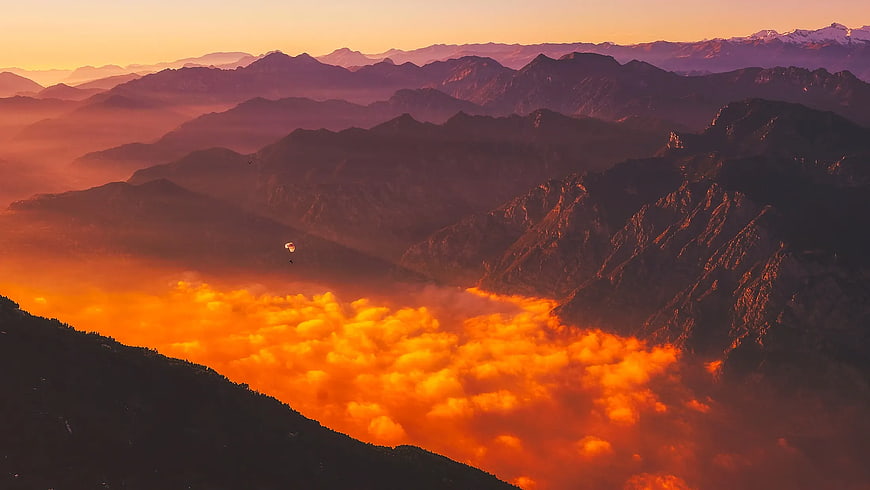 Paraglider soaring above sea of clouds at sunset