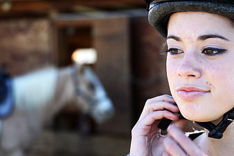 Young woman adjusting riding helmet with horse in background