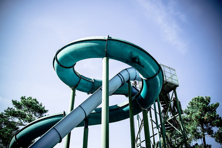 Low angle view of teal water slide loop against blue sky