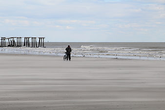 Man with bicycle on vast sandy beach near pier