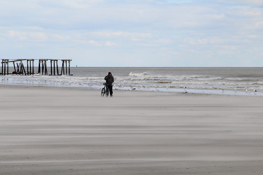 Man with bicycle on vast sandy beach near pier