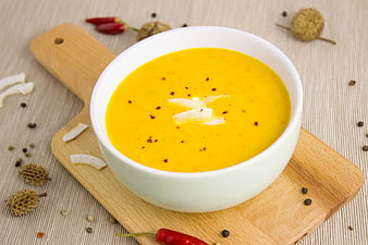 Creamy yellow pumpkin soup with coconut garnish on wooden board