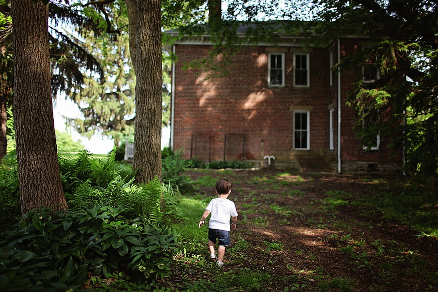 Toddler boy walking away toward brick house in backyard