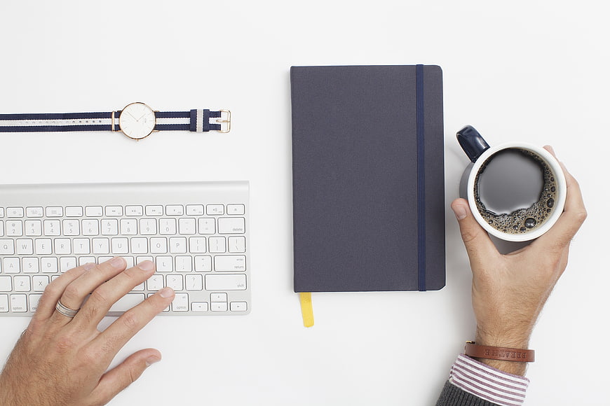 Flat lay of hands typing on keyboard with coffee and notebook