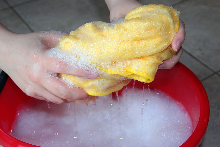 Hands wringing soapy yellow cloth over red bucket
