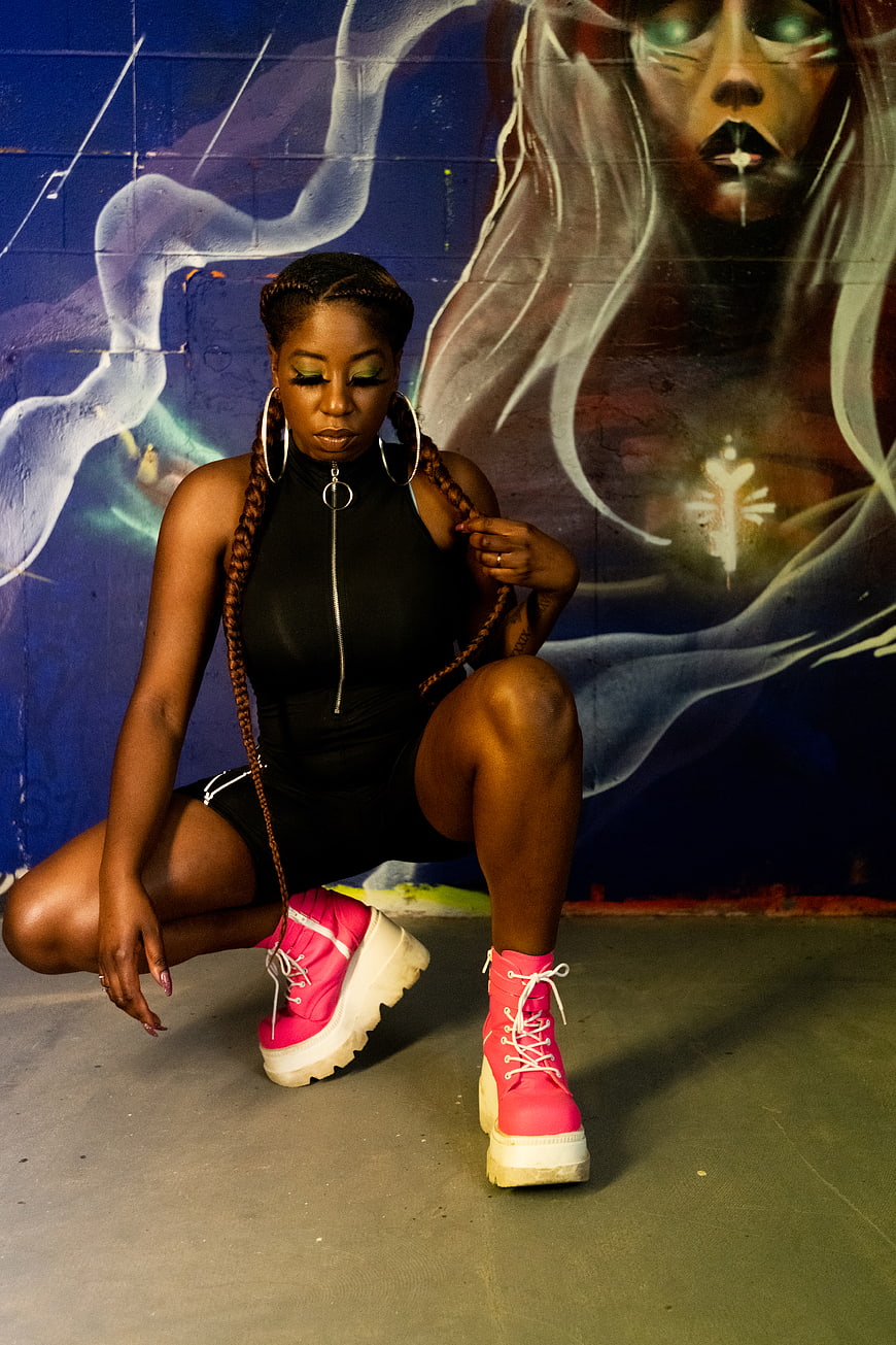 Stylish woman in pink boots posing against graffiti wall