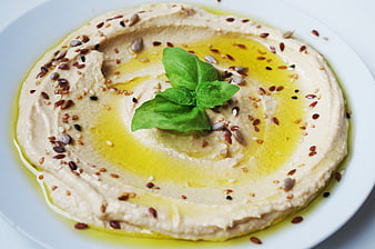 Hummus with olive oil, seeds, and fresh basil on a white plate