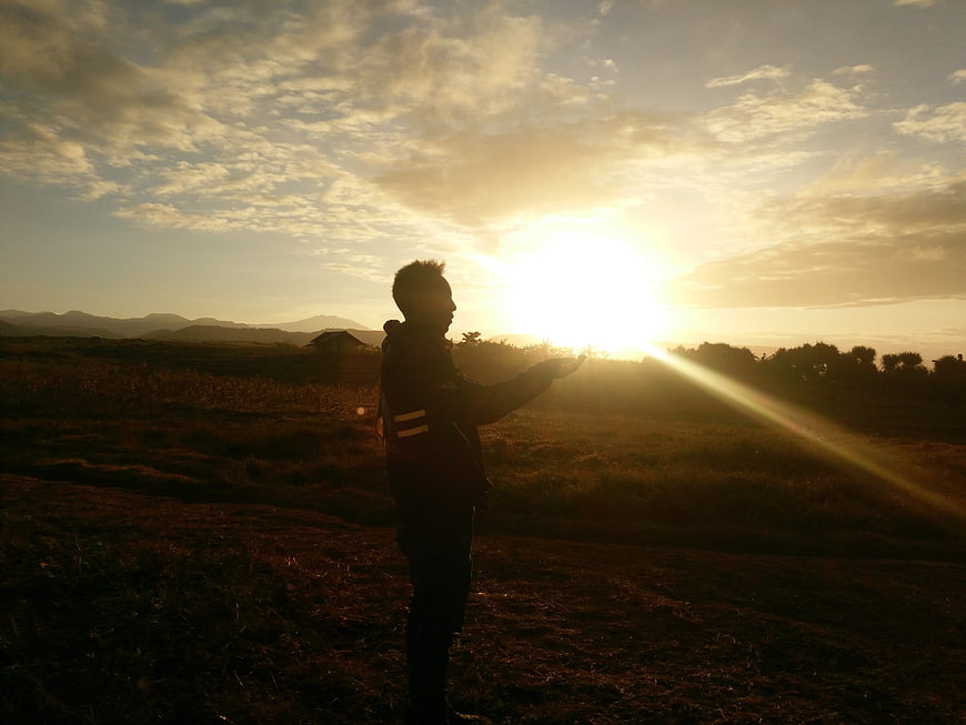 Silhouette of Man Holding Sun in Field at Sunset