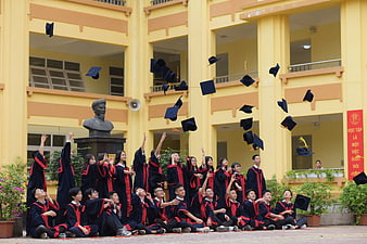 Graduation Students Tossing Caps In Front Of Yellow School Building