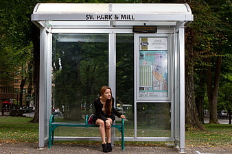 Young woman waiting alone at urban bus stop shelter