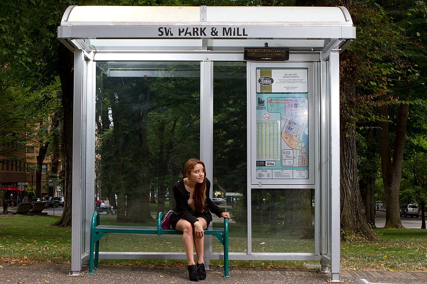 Young woman waiting alone at urban bus stop shelter