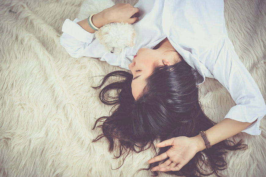 Woman Sleeping Peacefully with Small White Dog on Fur Rug