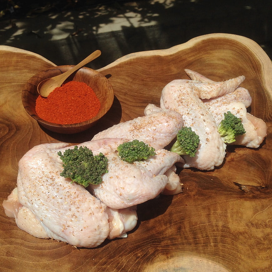 Raw seasoned chicken wings with broccoli and spices on wooden board
