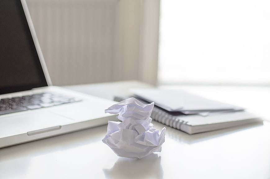 Crumpled paper ball on white desk with laptop and notebook