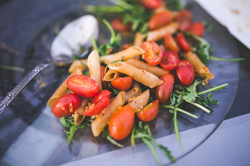 Penne pasta salad with cherry tomatoes and arugula on dark plate