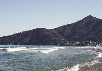 Coastal Beach Scene With Swimmers And Forested Hills