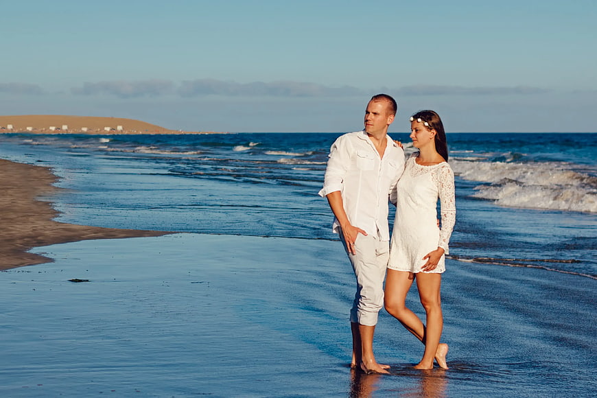 Couple in White Standing on Sandy Beach at Sunset