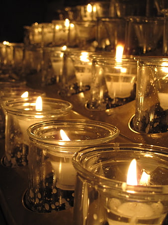Rows of lit votive candles in glass holders
