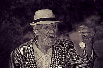 Senior man in fedora looking at pocket watch with smoke
