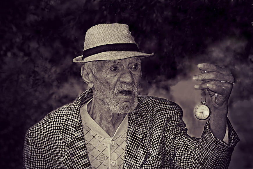 Senior man in fedora looking at pocket watch with smoke