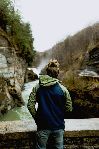 Man with bun looking at waterfall from stone bridge