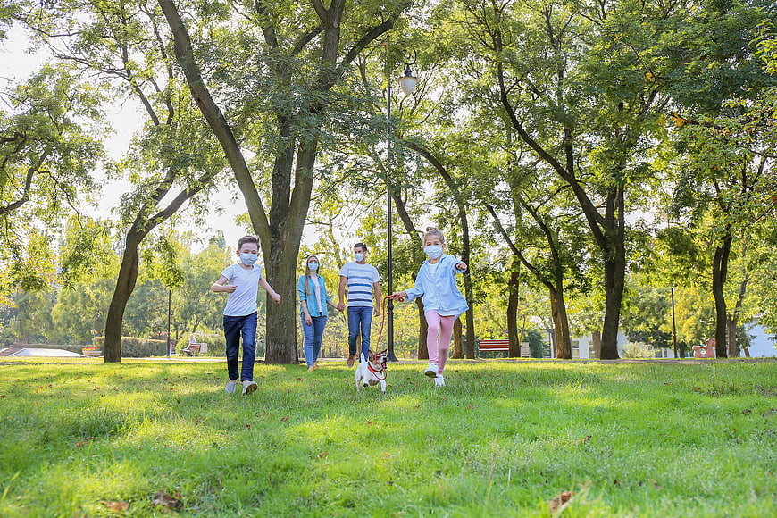 Family with dog running in park wearing face masks