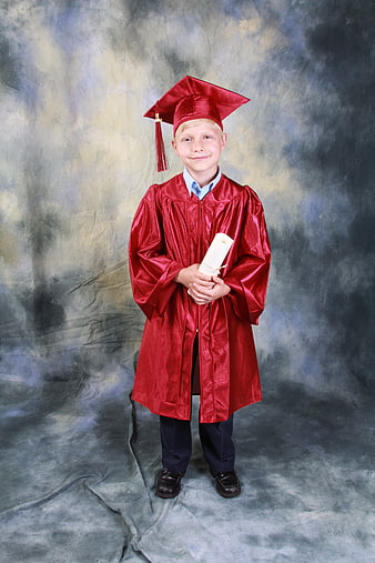 Young boy in red graduation gown holding diploma against studio backdrop